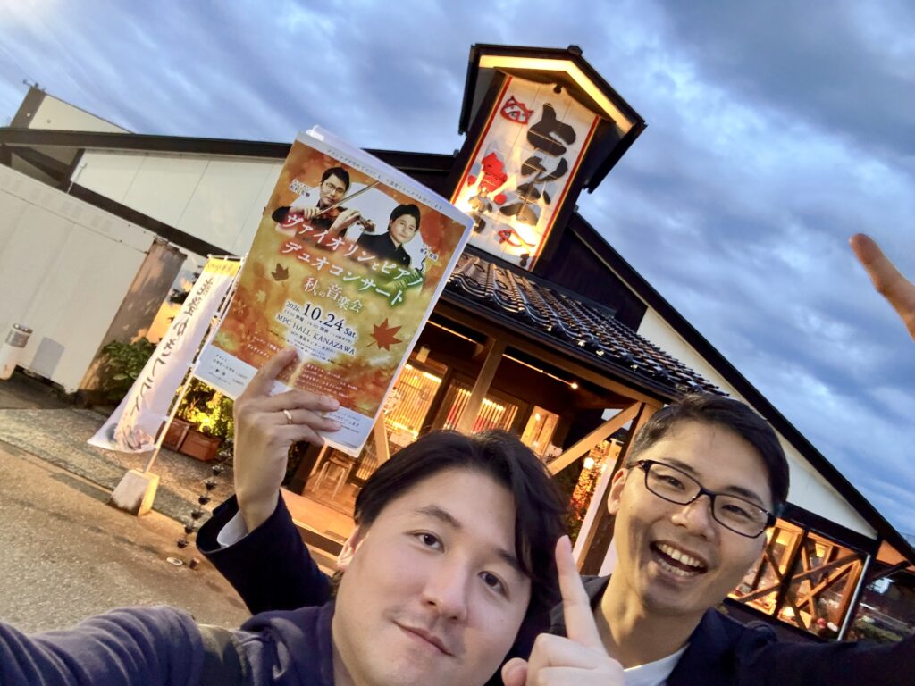 コンサート終演後に訪れた金沢かつぞう本店の前で、秋の音楽会のチラシを持って記念撮影する二人