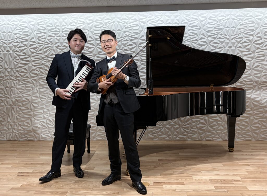 金沢の秋の音楽会終演後、グランドピアノの前でヴァイオリンとピアニカを持って記念撮影する出演者二人